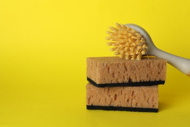 Photo of Sponges and cleaning brush on yellow background, closeup. Space for text