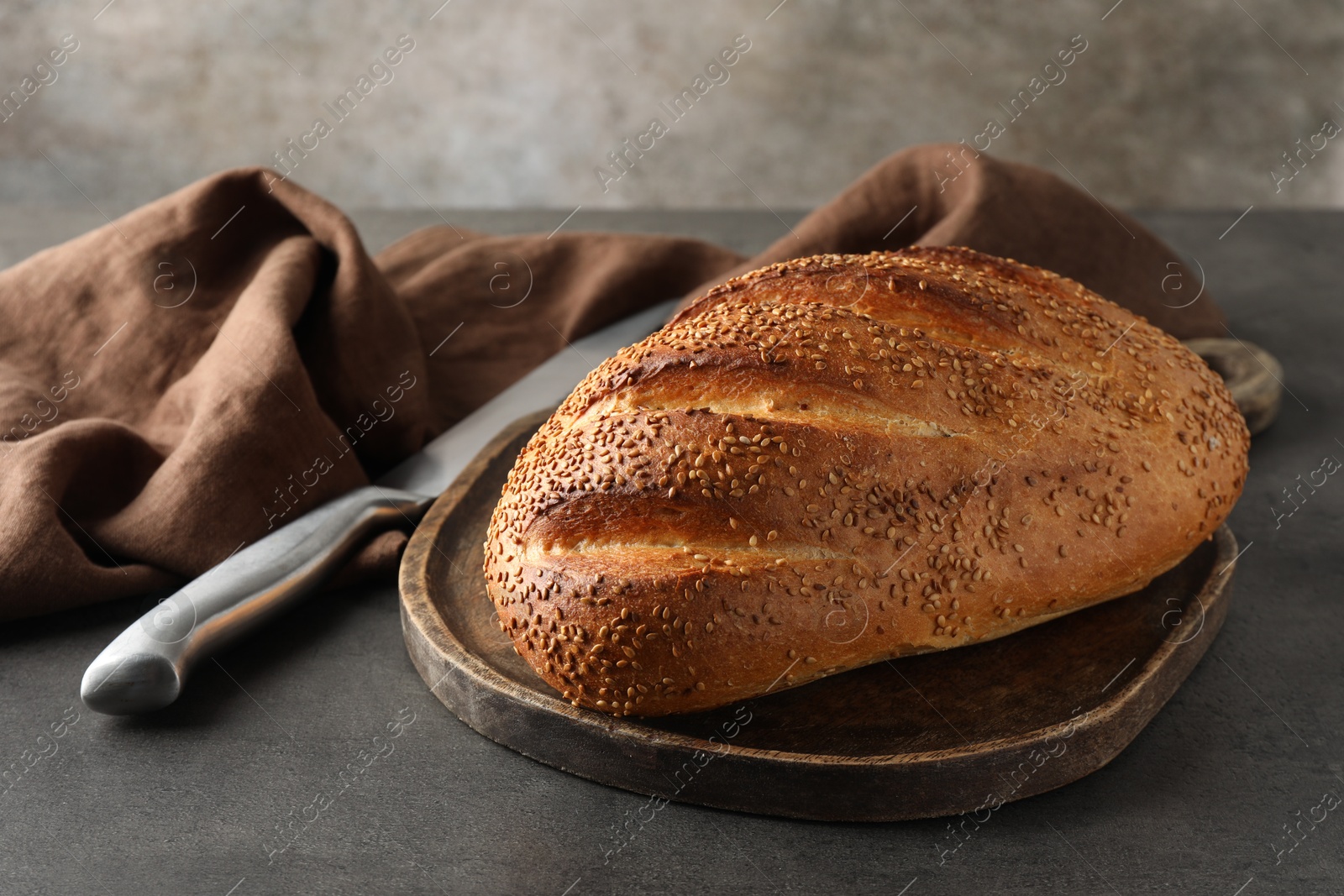 Photo of Freshly baked bread with seeds and knife on grey table, closeup