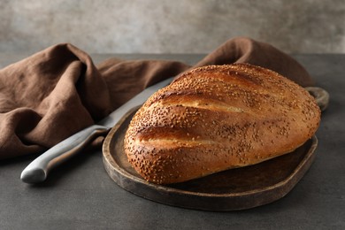 Photo of Freshly baked bread with seeds and knife on grey table, closeup