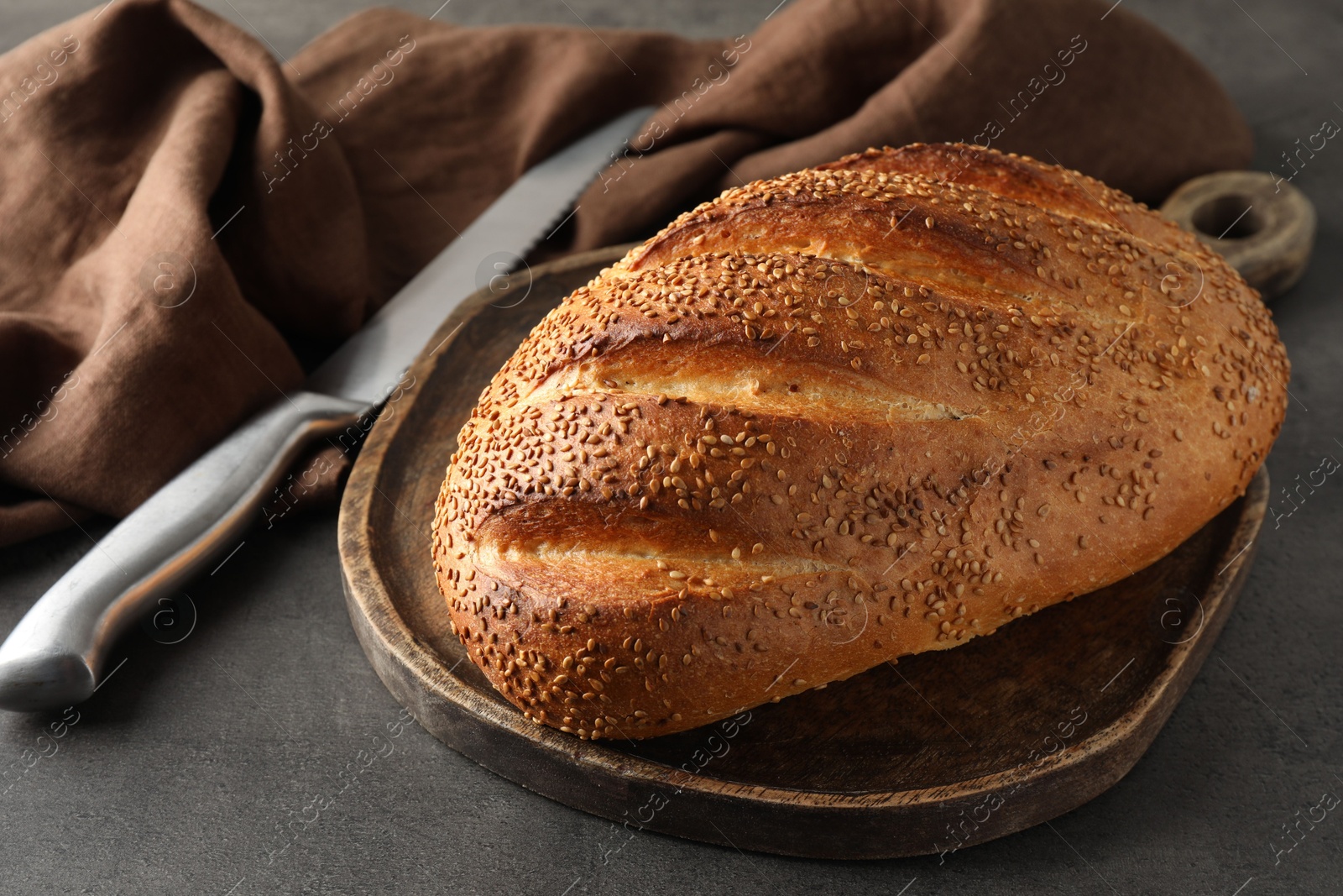 Photo of Freshly baked bread with seeds and knife on grey table, closeup