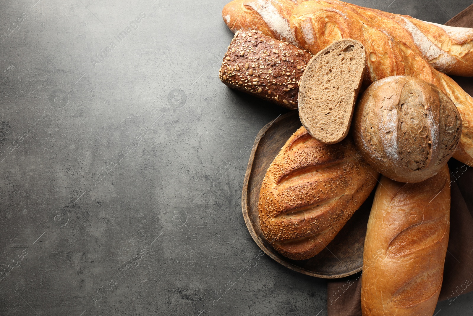 Photo of Different freshly baked bread loafs on grey table, flat lay. Space for text