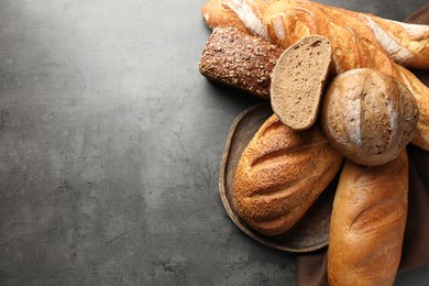 Photo of Different freshly baked bread loafs on grey table, flat lay. Space for text