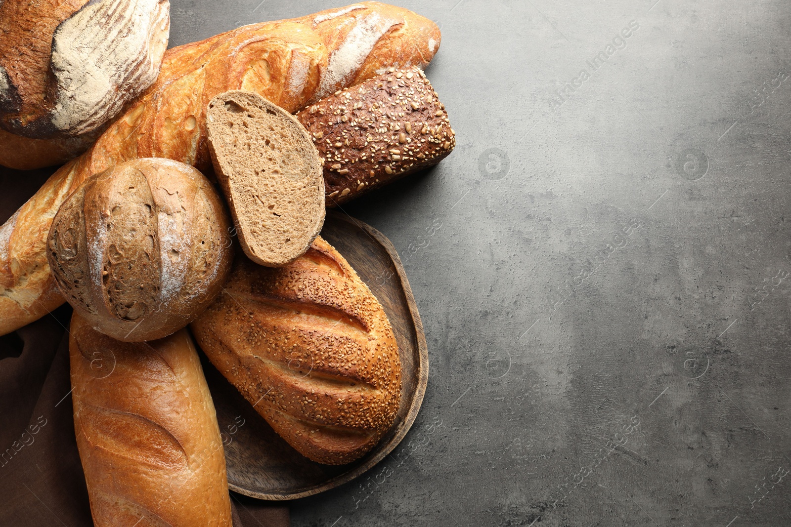 Photo of Different freshly baked bread loafs on grey table, flat lay. Space for text