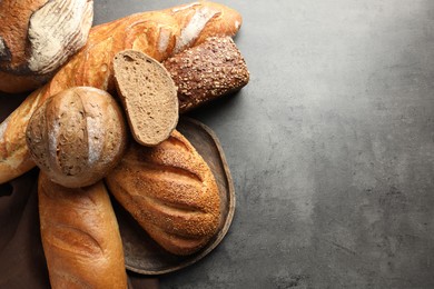 Photo of Different freshly baked bread loafs on grey table, flat lay. Space for text