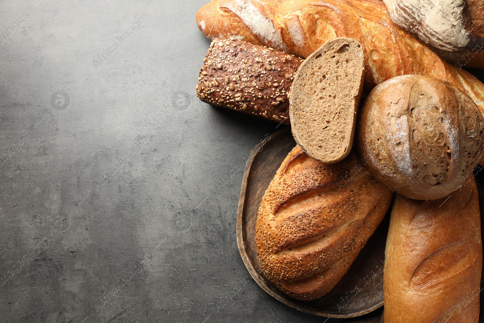 Photo of Different freshly baked bread loafs on grey table, flat lay. Space for text