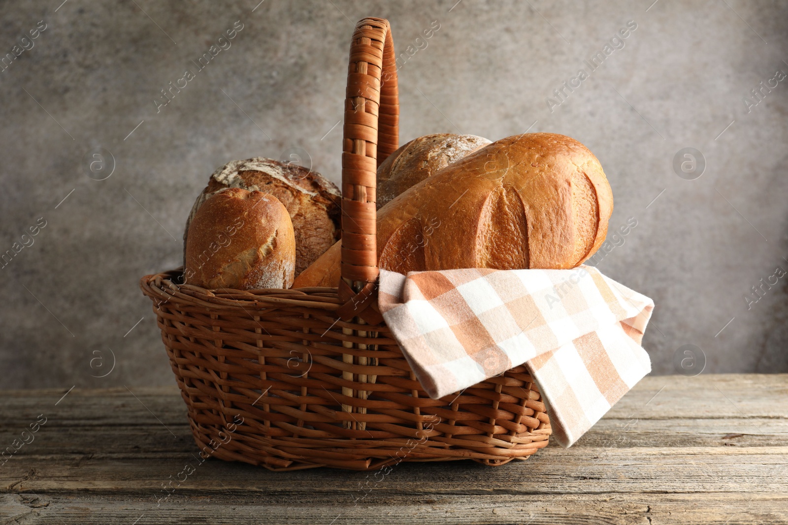 Photo of Different freshly baked bread loafs in wicker basket on wooden table