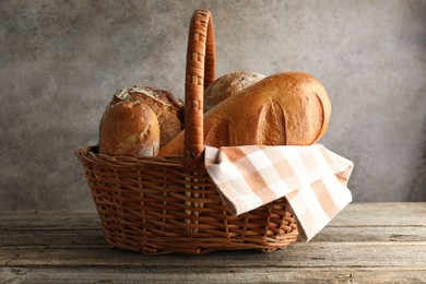 Photo of Different freshly baked bread loafs in wicker basket on wooden table