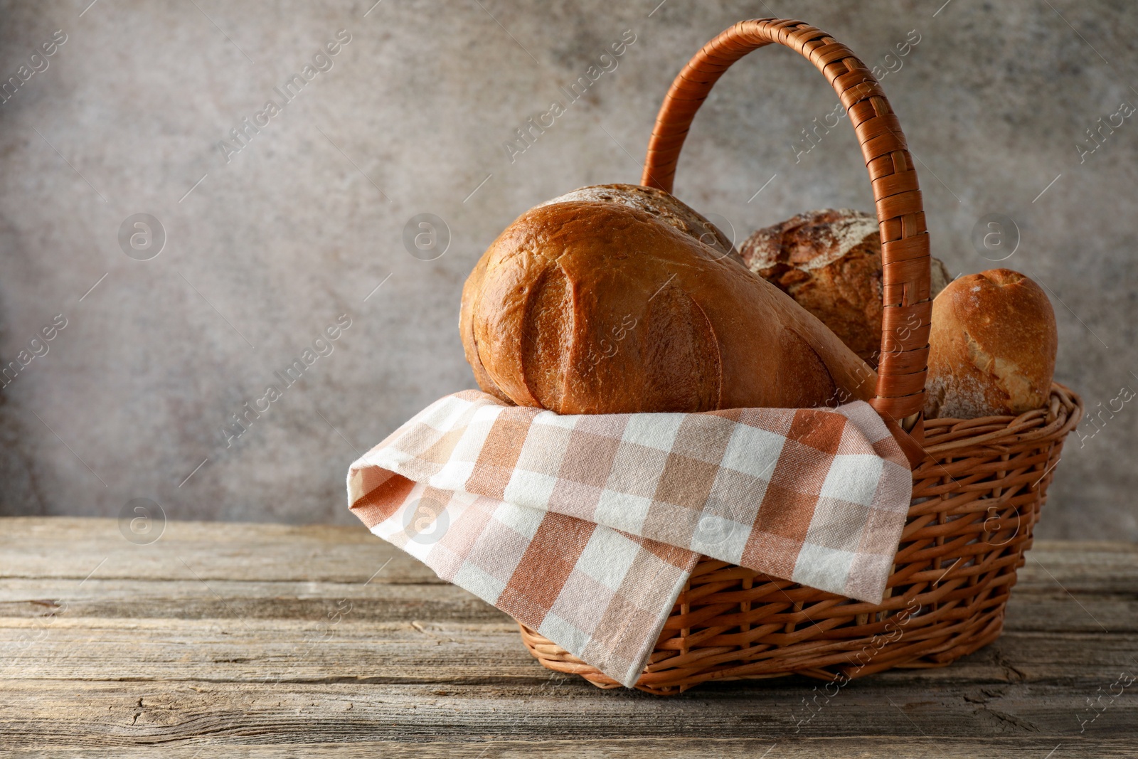 Photo of Different freshly baked bread loafs in wicker basket on wooden table, space for text