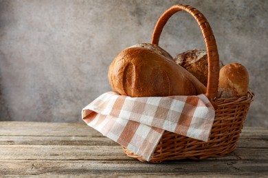 Photo of Different freshly baked bread loafs in wicker basket on wooden table, space for text