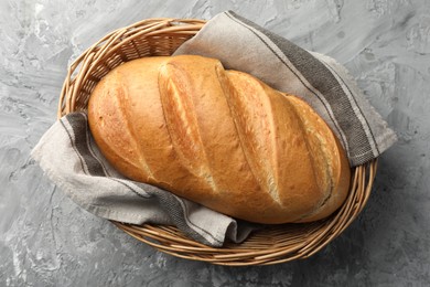 Photo of Freshly baked bread in wicker basket on grey table, top view