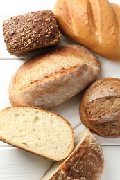 Photo of Whole and cut bread loafs on white wooden table, flat lay