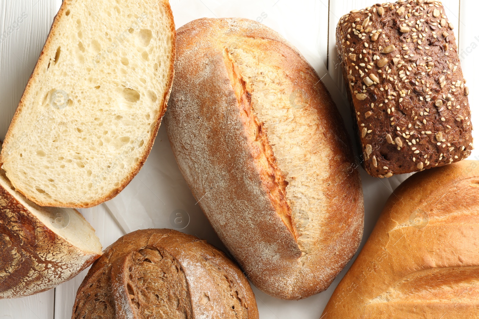 Photo of Whole and cut bread loafs on white wooden table, flat lay