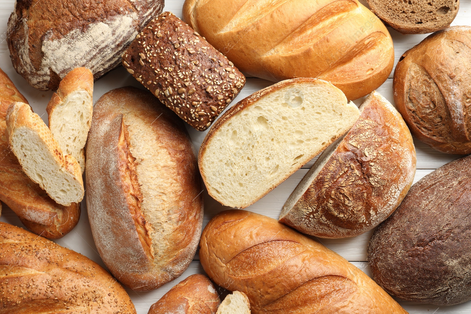 Photo of Whole and cut bread loafs on white wooden table, flat lay