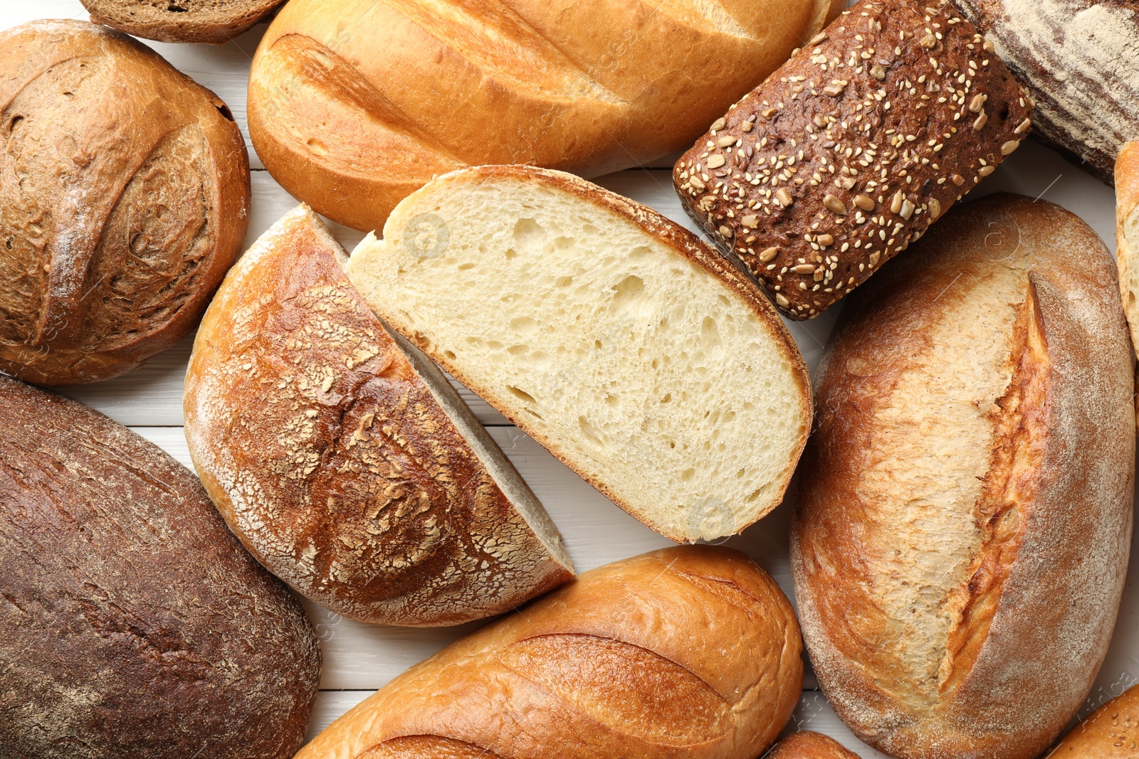 Photo of Whole and cut bread loafs on white wooden table, flat lay