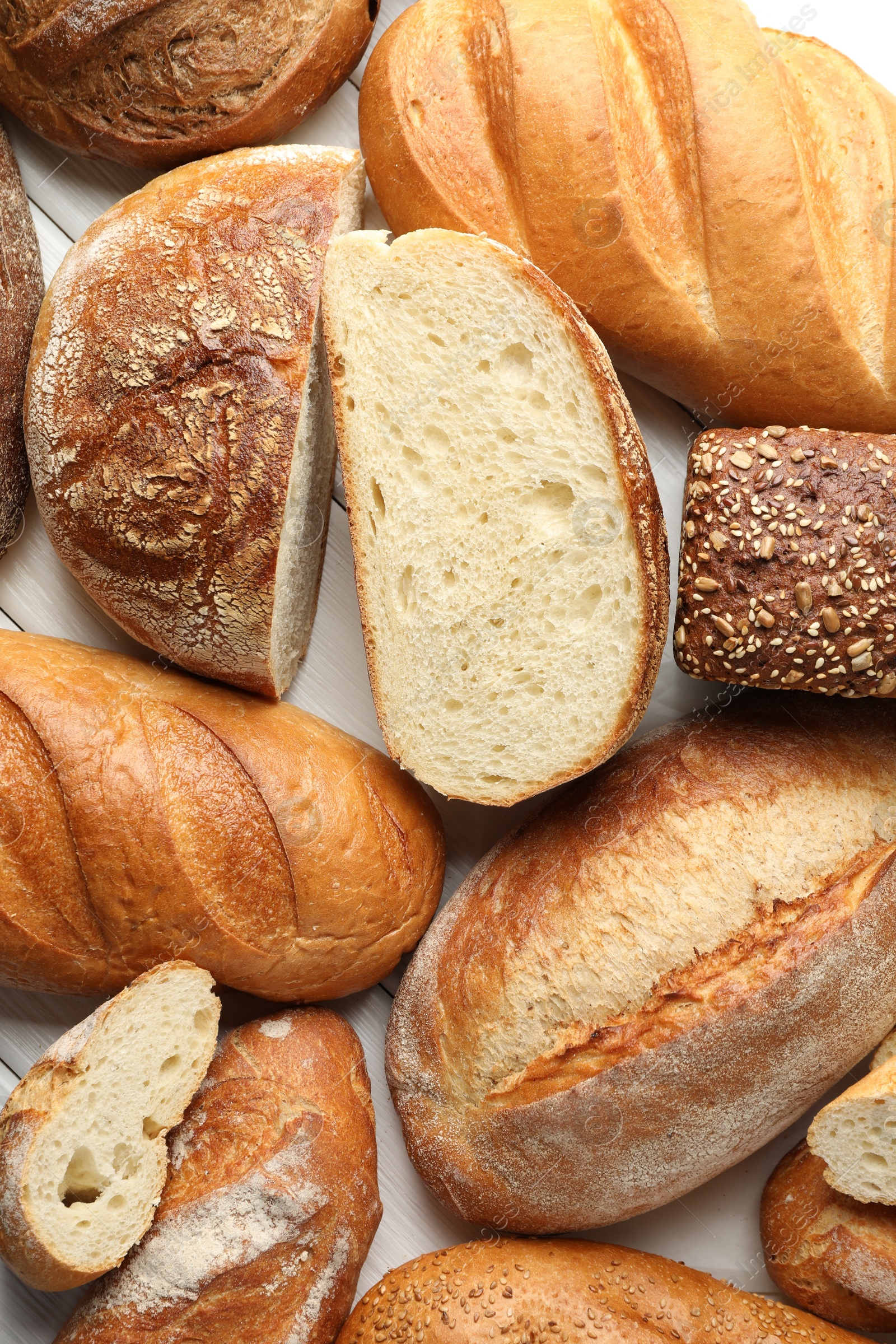 Photo of Whole and cut bread loafs on white table, flat lay