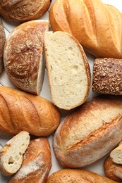 Photo of Whole and cut bread loafs on white table, flat lay