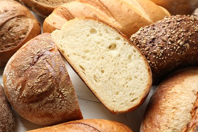 Photo of Whole and cut bread loafs on white table, closeup