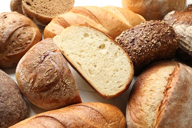 Photo of Whole and cut bread loafs on white table, closeup