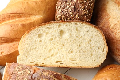 Photo of Whole and cut bread loafs on white table, closeup