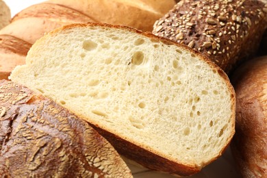 Photo of Whole and cut bread loafs on white table, closeup