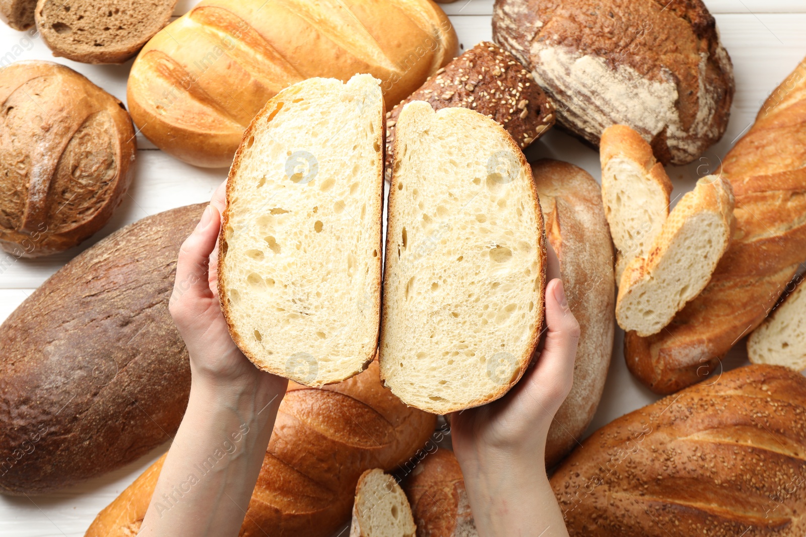 Photo of Woman with pieces of fresh bread over different other loafs at white table, top view