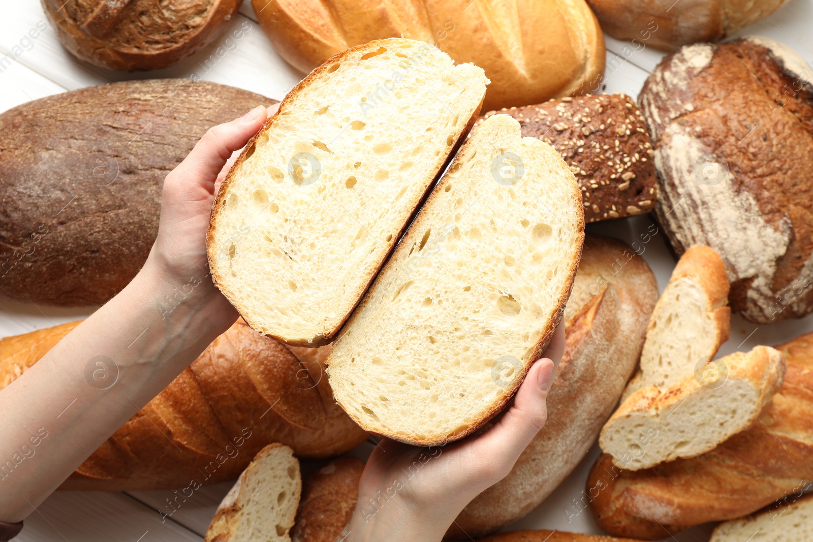 Photo of Woman with pieces of fresh bread over different other loafs at white table, top view