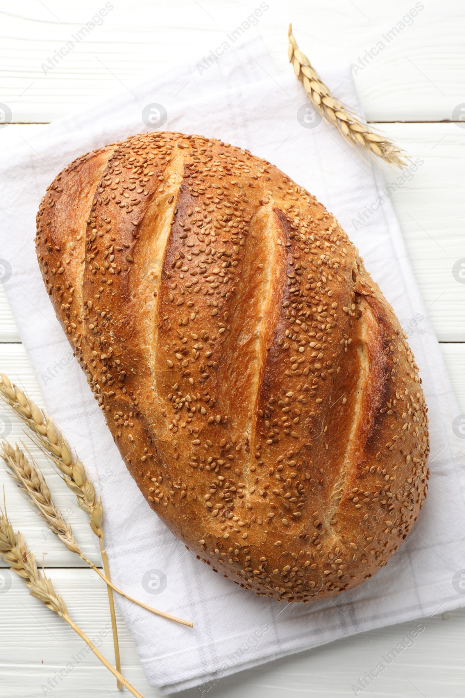 Photo of Loaf of bread with sesame seeds and spikes on white wooden table, flat lay