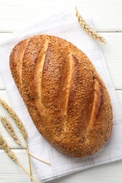 Photo of Loaf of bread with sesame seeds and spikes on white wooden table, flat lay