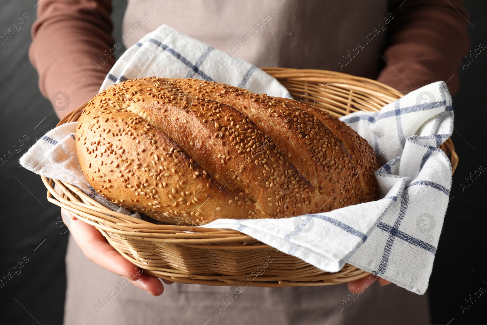 Photo of Woman with loaf of freshly baked bread on black background, closeup