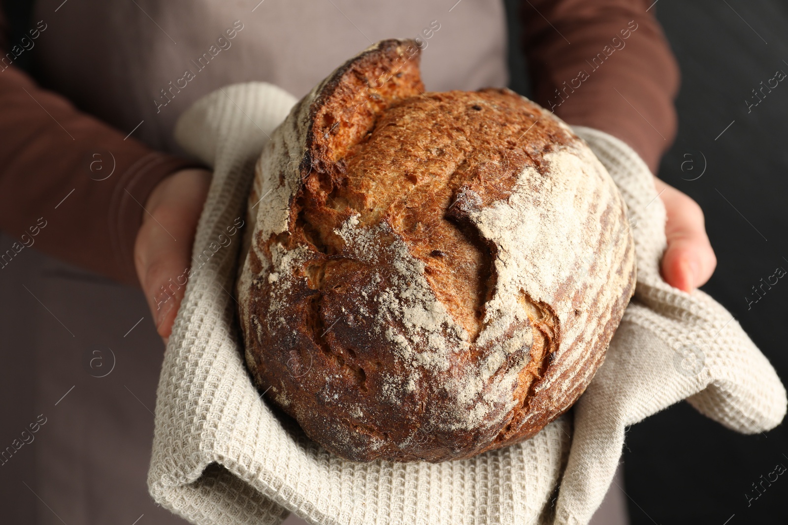 Photo of Woman with loaf of freshly baked bread on black background, closeup