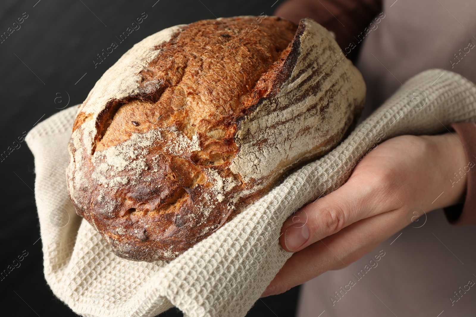 Photo of Woman with loaf of freshly baked bread on black background, closeup