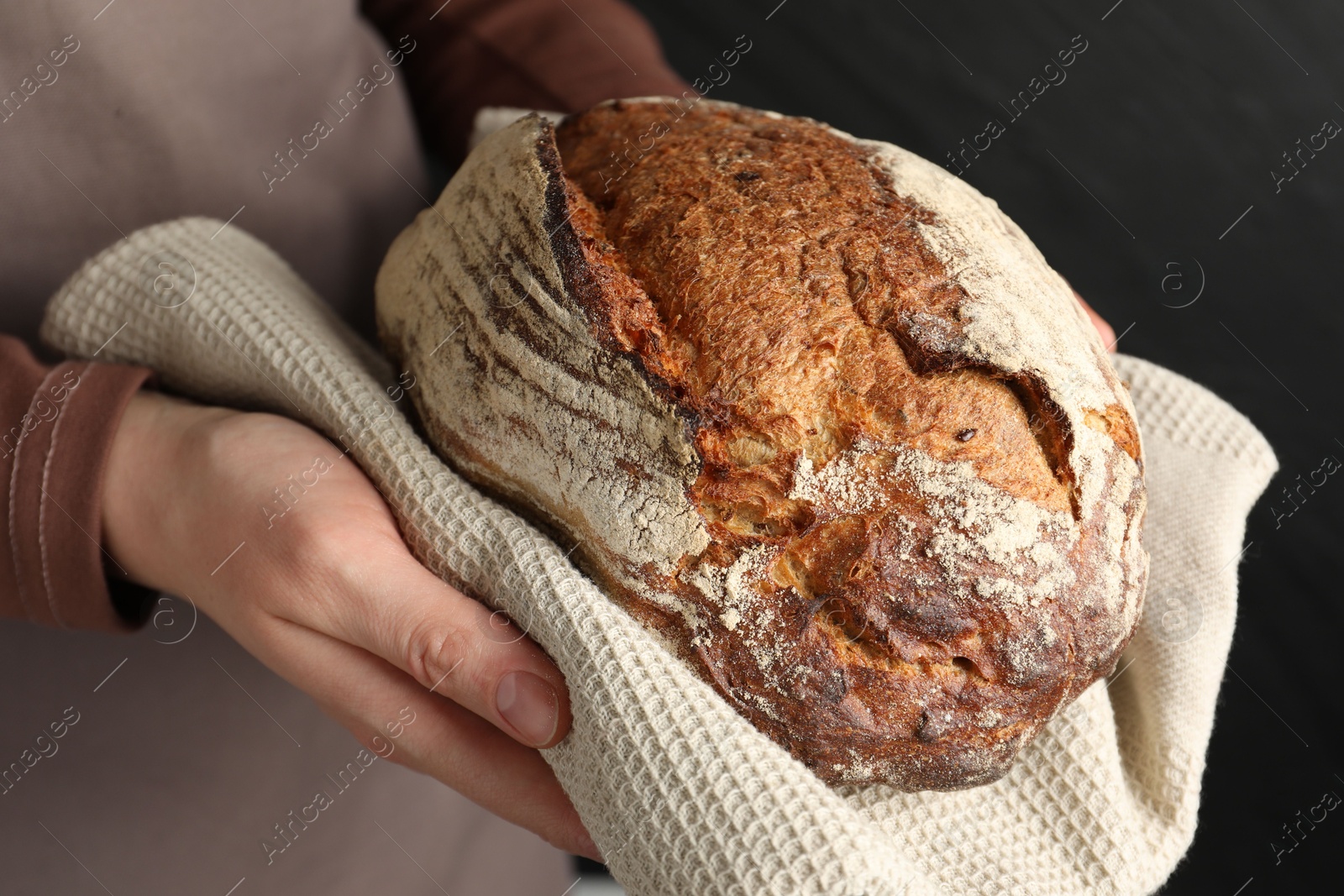 Photo of Woman with loaf of freshly baked bread on black background, closeup