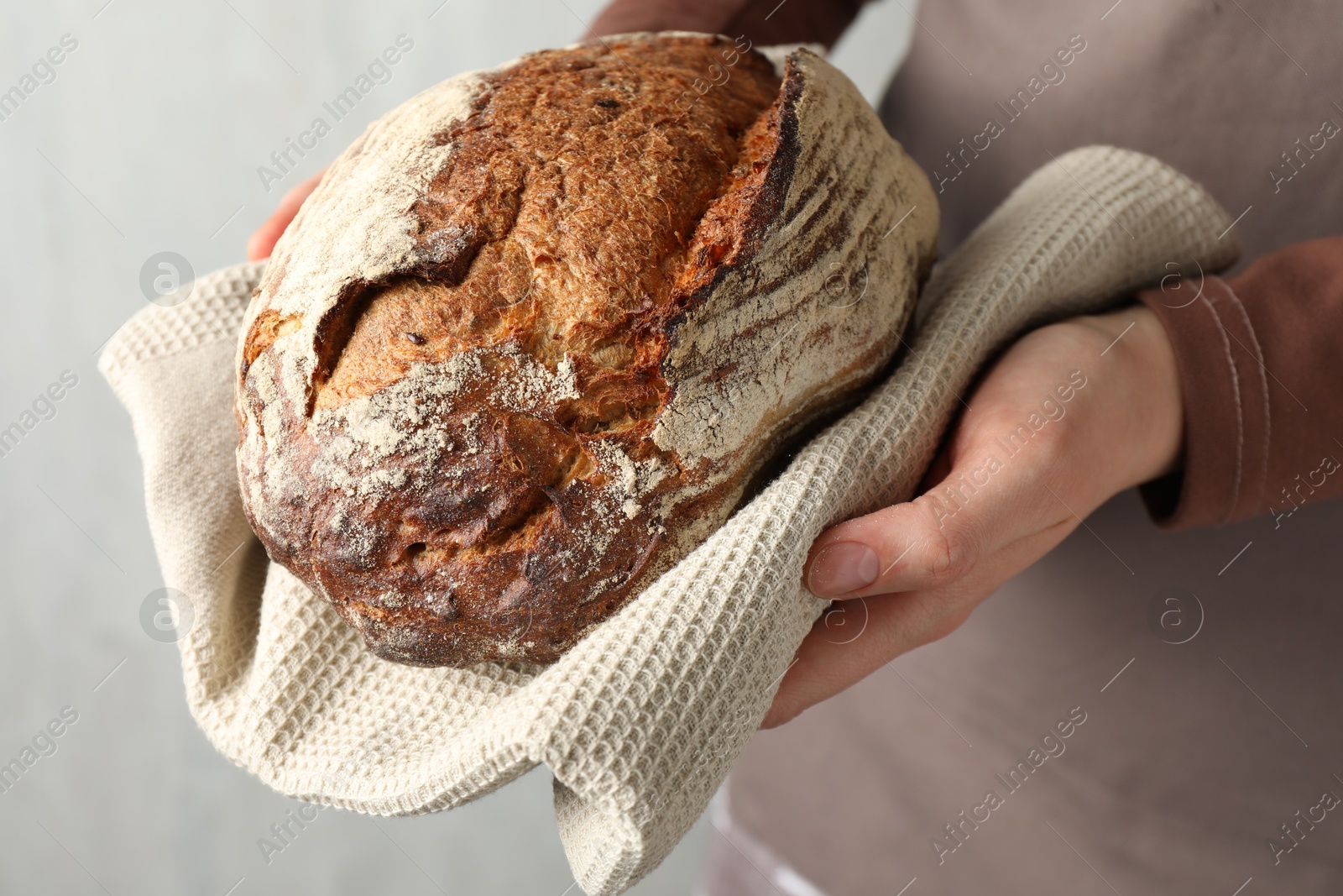 Photo of Woman with loaf of freshly baked bread on light background, closeup