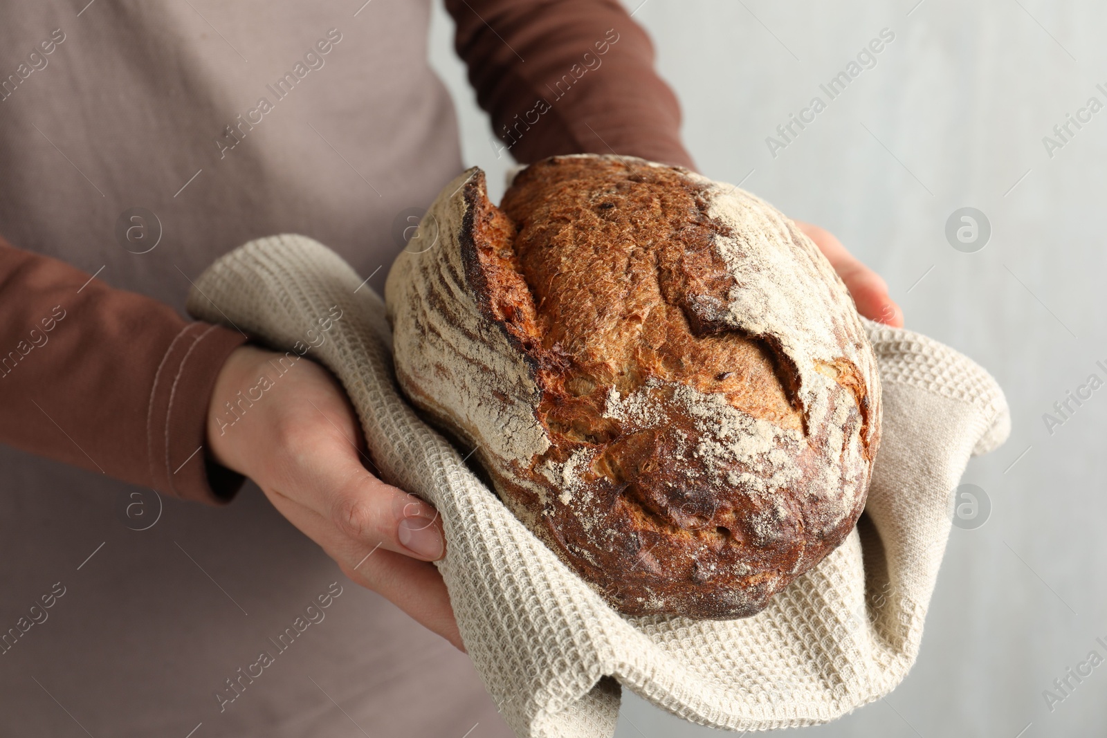 Photo of Woman with loaf of freshly baked bread on light background, closeup