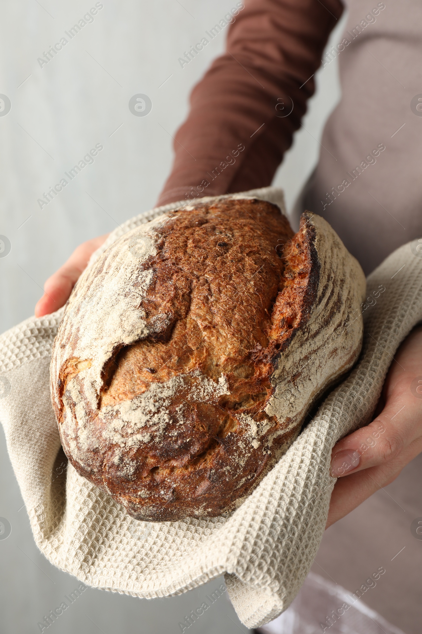 Photo of Woman with loaf of freshly baked bread on light background, closeup