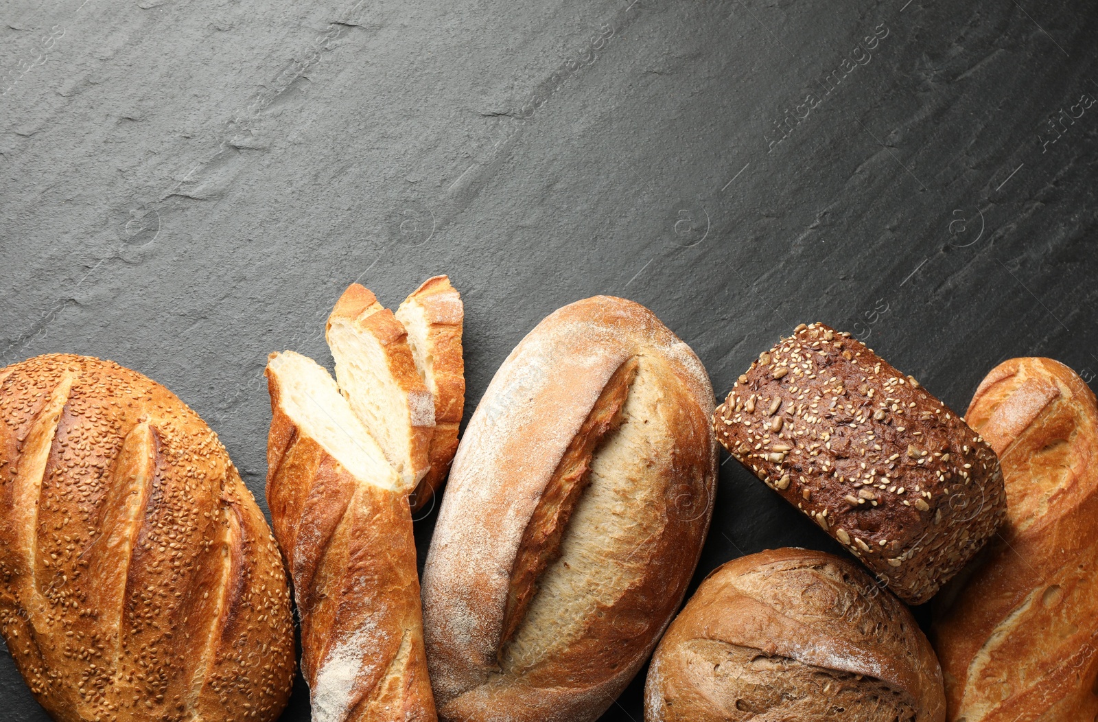 Photo of Loafs of different bread on black background, flat lay. Space for text