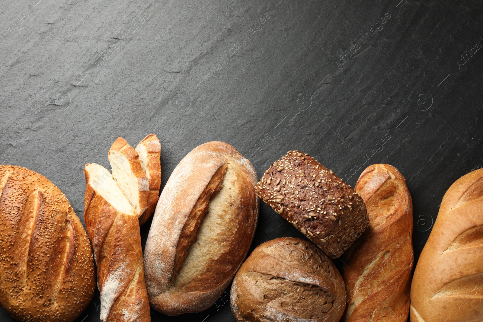 Photo of Loafs of different bread on black background, flat lay. Space for text