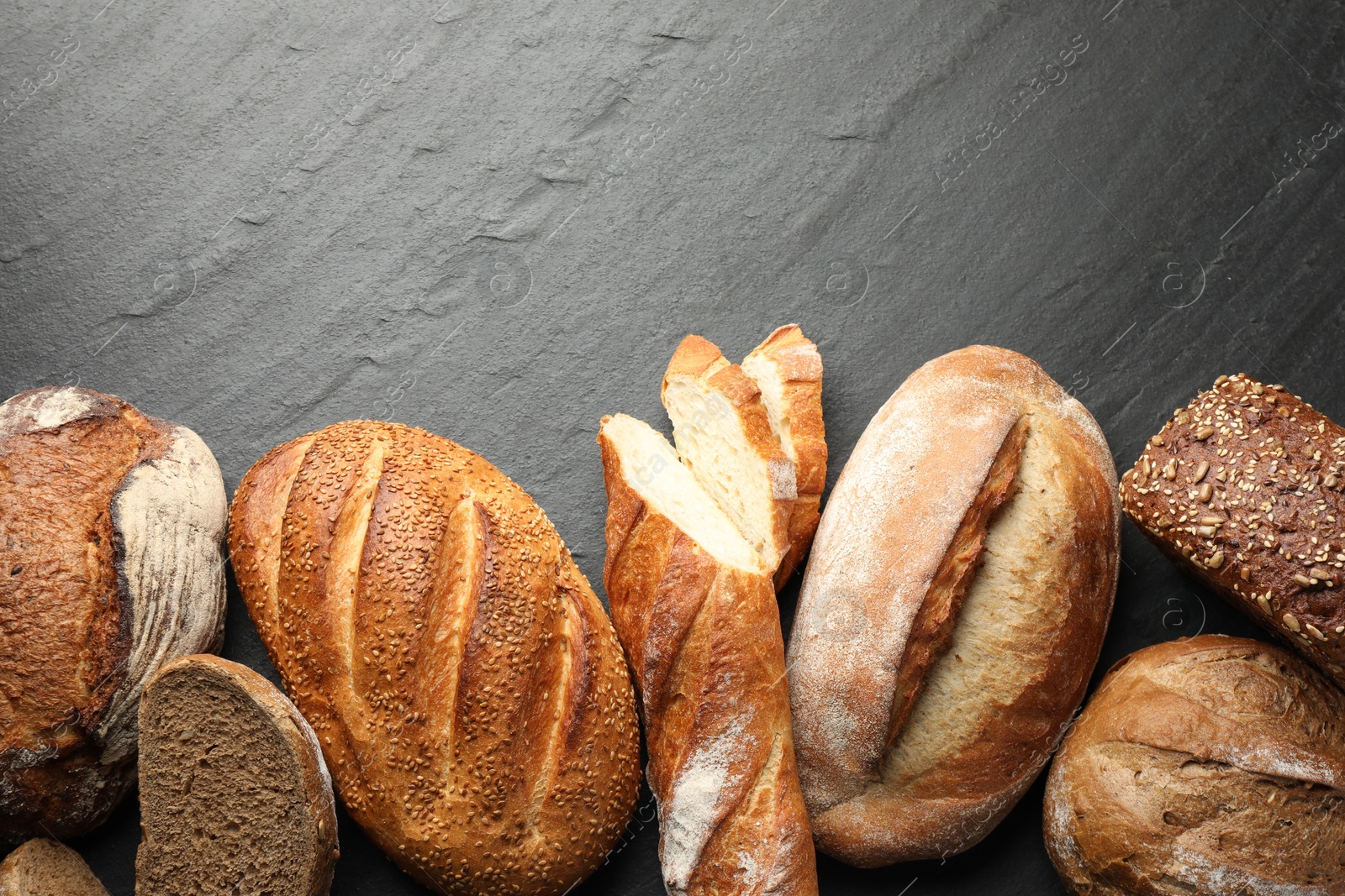 Photo of Loafs of different bread on black background, flat lay. Space for text