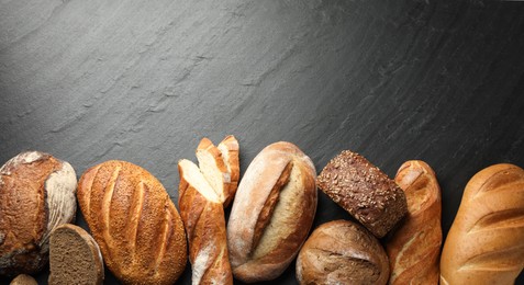 Photo of Loafs of different bread on black background, flat lay. Space for text