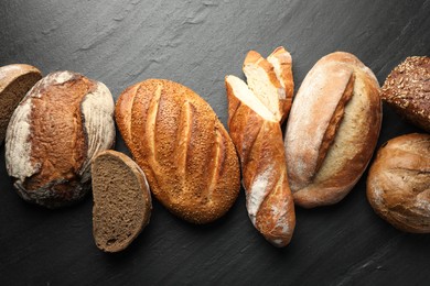 Photo of Loafs of different bread on black background, flat lay