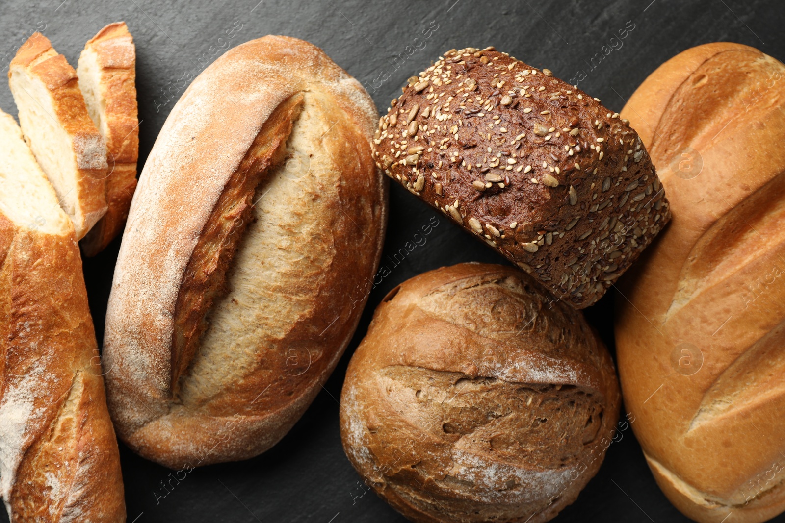 Photo of Loafs of different bread on black background, flat lay