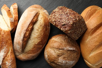 Photo of Loafs of different bread on black background, flat lay