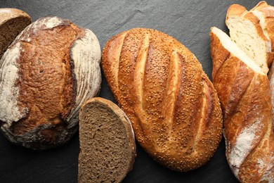 Photo of Loafs of different bread on black background, flat lay