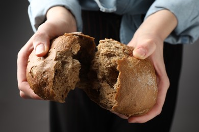 Photo of Woman breaking loaf of fresh rye bread on grey background, closeup