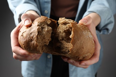 Photo of Woman breaking loaf of fresh rye bread on grey background, closeup