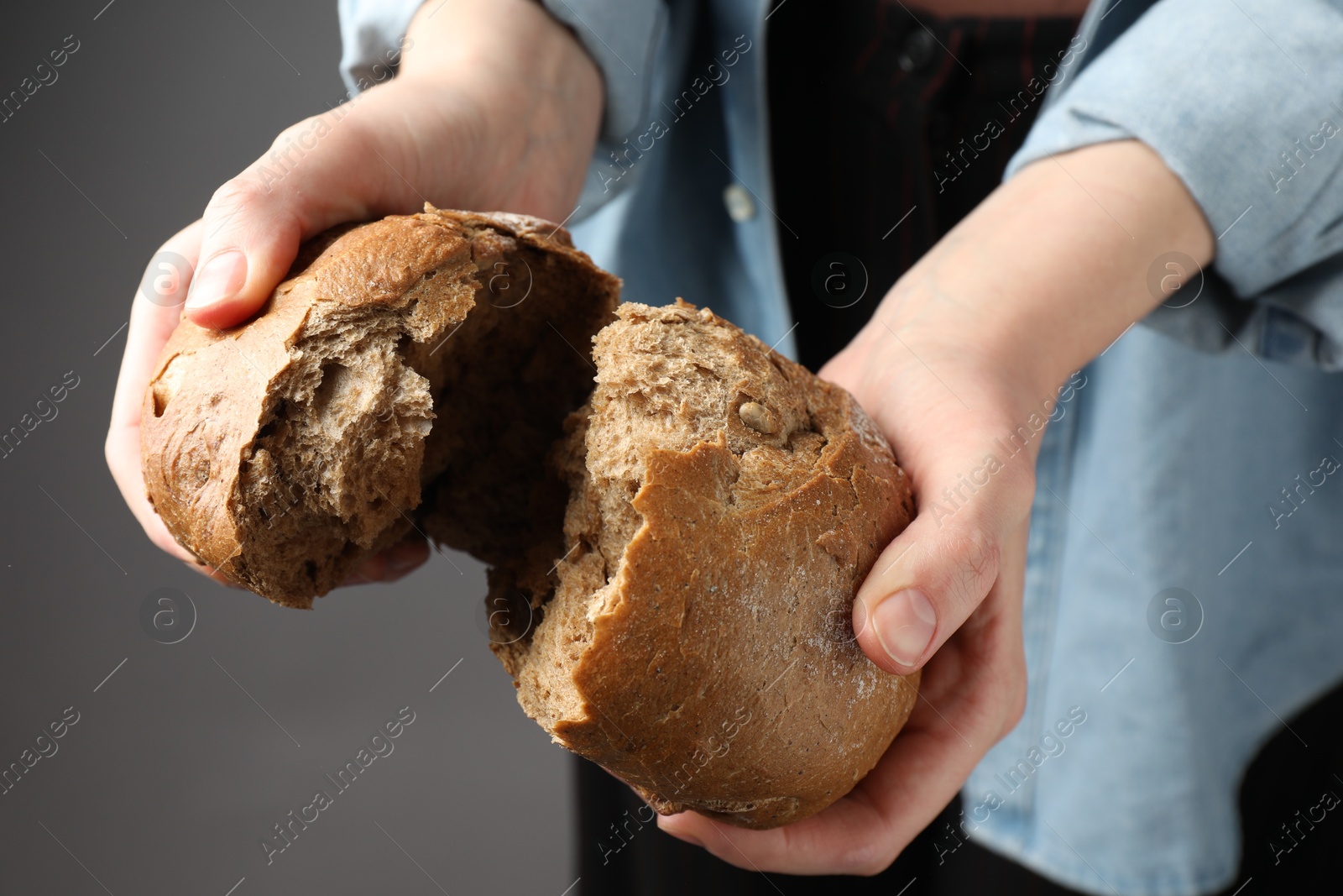 Photo of Woman breaking loaf of fresh rye bread on grey background, closeup