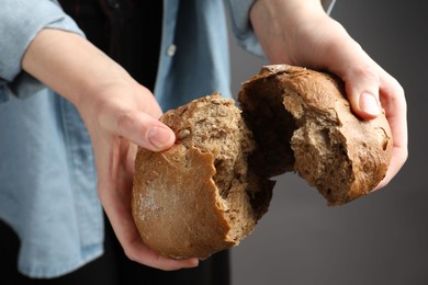 Photo of Woman breaking loaf of fresh rye bread on grey background, closeup