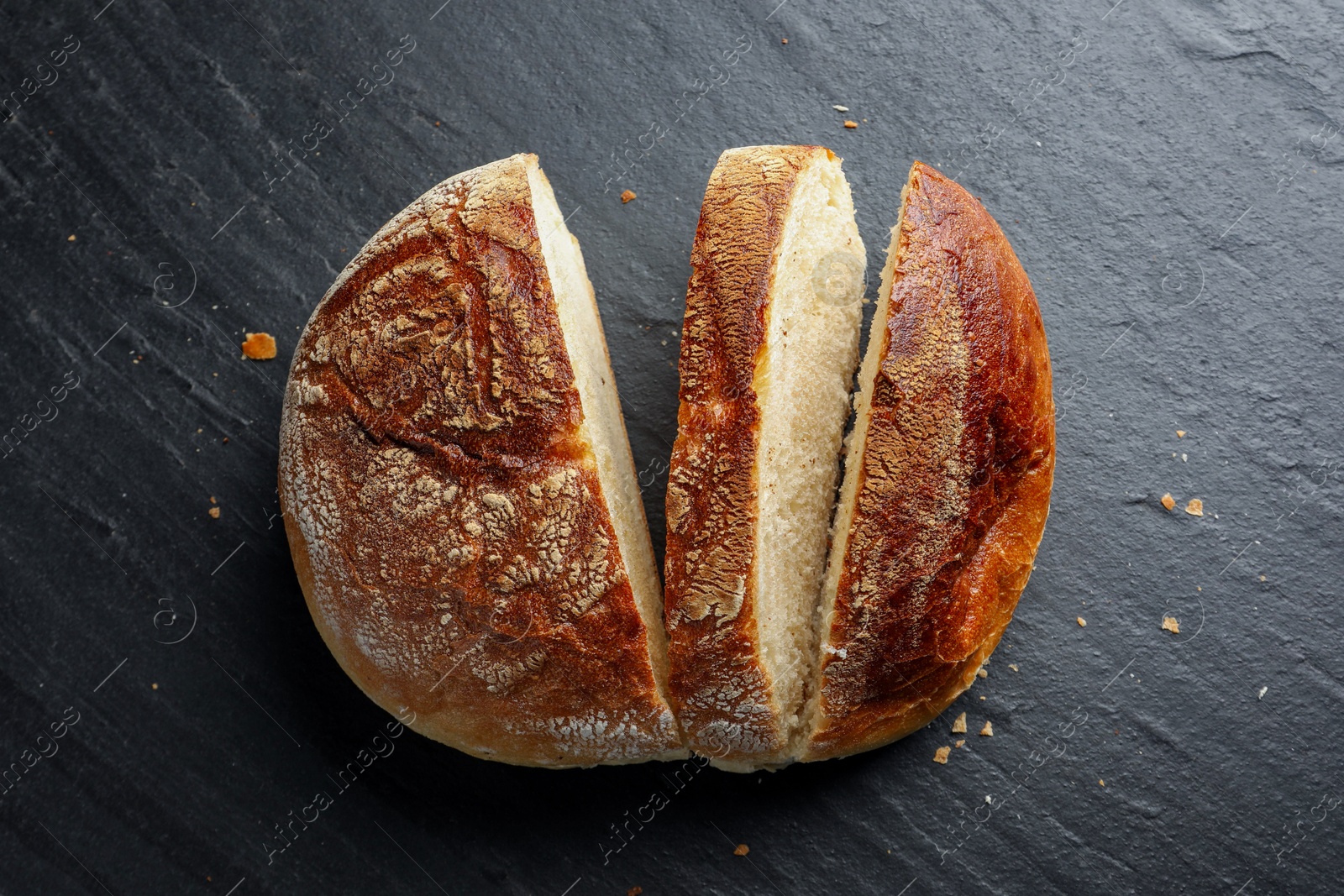 Photo of Cut loaf of fresh bread on black background, top view