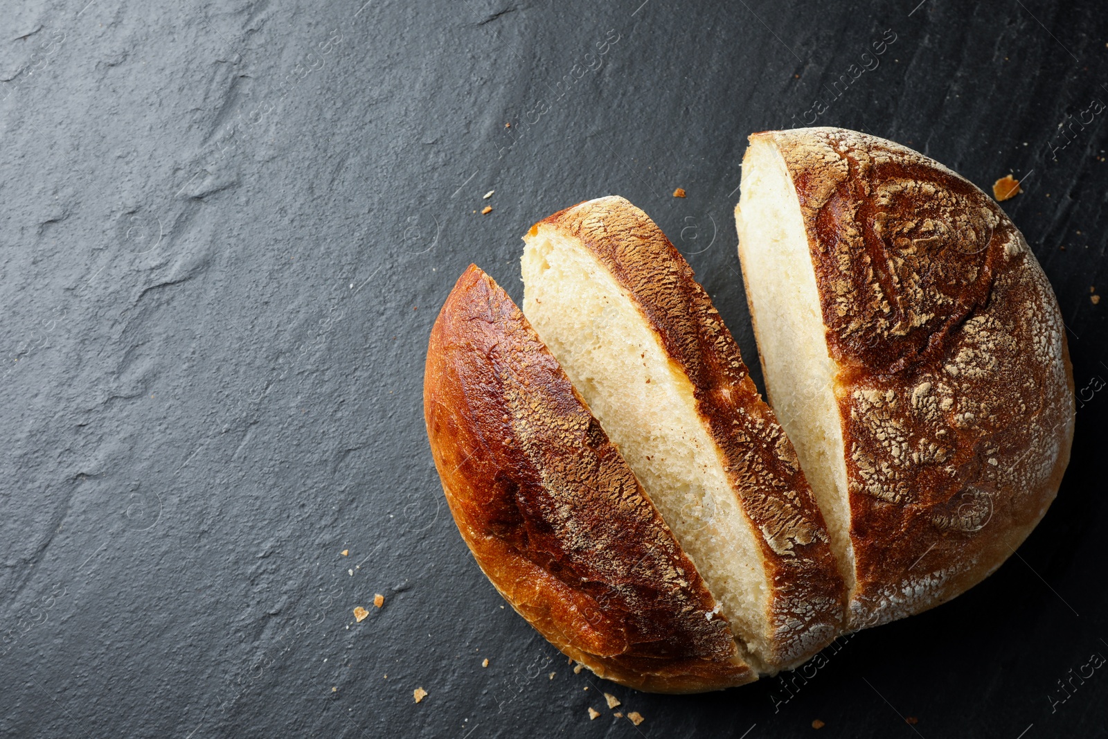 Photo of Cut loaf of fresh bread on black background, top view. Space for text