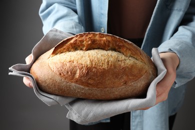 Photo of Woman with loaf of freshly baked bread on grey background, closeup